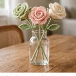 Crochet lisianthus roses in sage green, cream, and blush pink in a glass vase