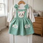 Kitty cat pinafore dress in mint green crochet hanging on a nursery closet door