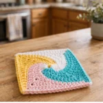 Colorful crochet pinwheel square motif on a wooden kitchen table