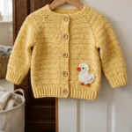 Sunny yellow baby cardigan with duck applique laid on a table
