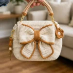 Cream white crocheted bow handbag with caramel edging, striped handle, and gold hardware